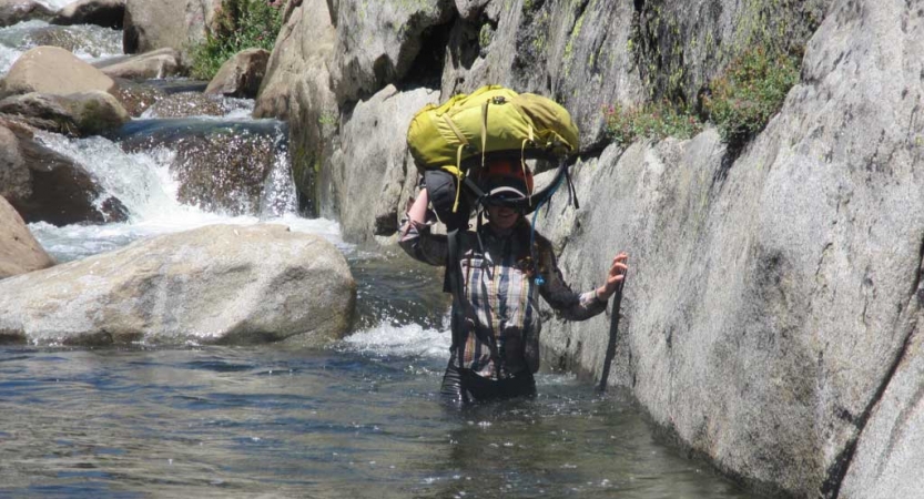 a person carries their backpack on their head as they wade through waist-deep water